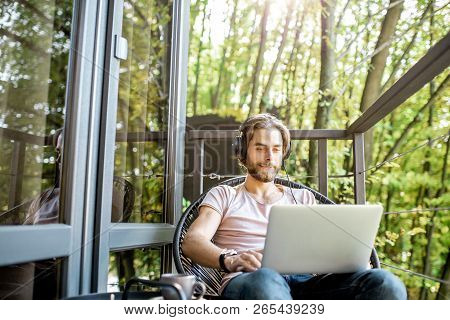 Poortrait Of A Handsome Man Working With Laptop On The Balcony Of The House In The Beautiful Green F