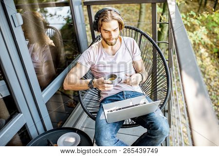Poortrait Of A Handsome Man Working With Laptop On The Balcony Of The House In The Beautiful Green F
