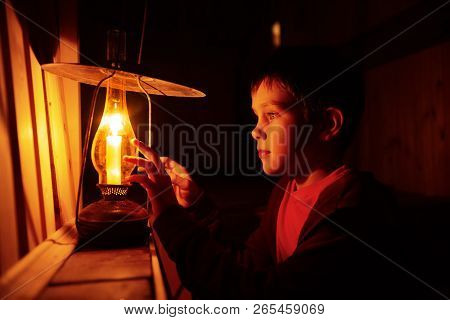 Boy Reading In The Light Of An Old Lamp. The Child Sitting On A Dark Staircase With A Book