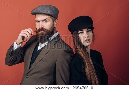 Vintage Retro Couple On Red Wall. Old Style Hat On Bearded Man And Black Fashion Cap On Beauty Woman