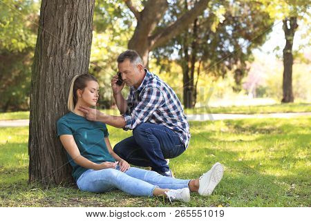 Passerby Calling Ambulance While Checking Pulse Of Unconscious Woman Outdoors. First Aid