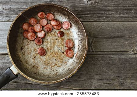 Frying Pan With Fried Pieces Of Sausages On An Old Wooden Table
