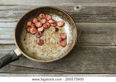 Frying Pan With Fried Pieces Of Sausages On An Old Wooden Table
