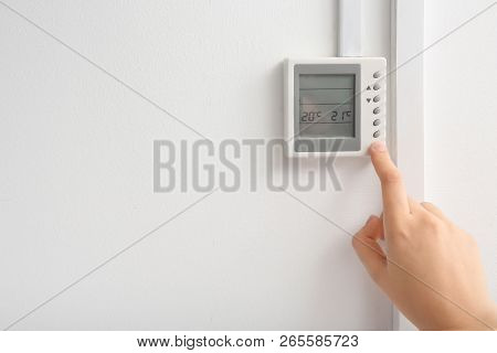 Woman Adjusting Thermostat On White Wall, Closeup. Heating System