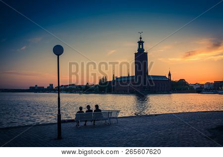 Silhouette Of Women Sitting On Bench At Promenade Quay Bank Of Lake Malaren Looking At Stockholm Cit