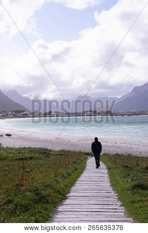 Young Man Standing At The Beach With Clouds And Blue Sky The Sea At Ramberg Lofoten Islands, Norway 