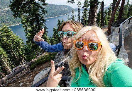 Two Young Adult Woman Take A Selfie At Lake Tahoe Emerald Bay, Wearing Beach Sunglasses And Making D