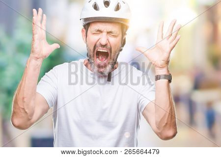 Middle age senior hoary cyclist man wearing bike safety helment isolated background celebrating mad and crazy for success with arms raised and closed eyes screaming excited. Winner concept