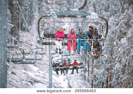 Happy family skier and snowboarder lifting on the chairlift at ski resort