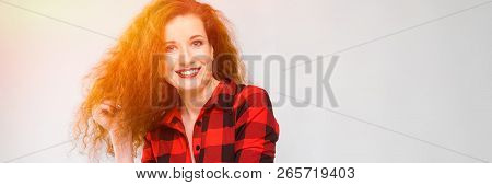 Young Red-haired Girl In A Red Checkered Shirt. Young Girl Holds Her Hair With Her Hand