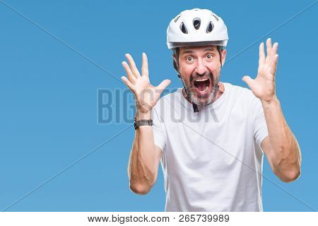 Middle age senior hoary cyclist man wearing bike safety helment isolated background celebrating crazy and amazed for success with arms raised and open eyes screaming excited. Winner concept