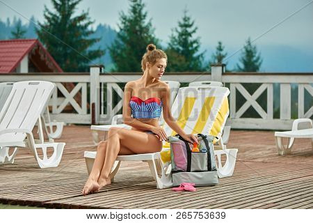 Sweet Woman, Wearing In Striped Swimsuit, Getting Sunblock Cream From Gray Backpack, Sitting On Chai
