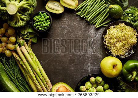 Round green healthy food composition with avocado, broccoli, apple, smoothie, cucomber, asparagus, kiwi, bean. Placed on dark background. Top view with copy space in the middle.