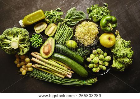Green healthy food composition with avocado, broccoli, apple smoothie, cucomber, asparagus, kiwi and bean. Placed on dark background. Top view.