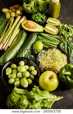 Green healthy food composition with avocado, broccoli, apple smoothie cucomber asparagus kiwi bean. Placed on dark background. Top view.