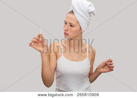 Young Woman Stands And Holds Ear Sticks In Hands. She Looks At Them And Wonderes. Model Wer White T-
