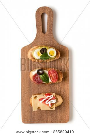 Open faced sandwich canape or crostini on a wooden serving board isolated on white background closeup. Top view.