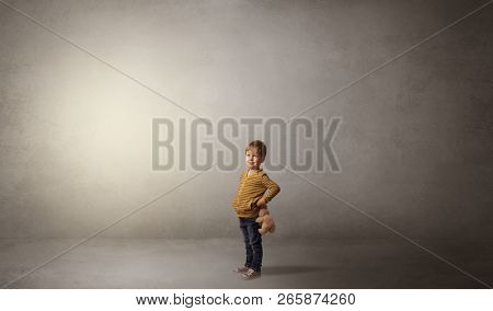 Little waggish kid staying alone in a big empty room with his plush