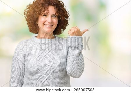 Beautiful middle ager senior woman wearing winter sweater over isolated background smiling with happy face looking and pointing to the side with thumb up.