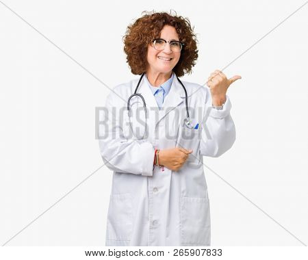 Middle ager senior doctor woman over isolated background smiling with happy face looking and pointing to the side with thumb up.