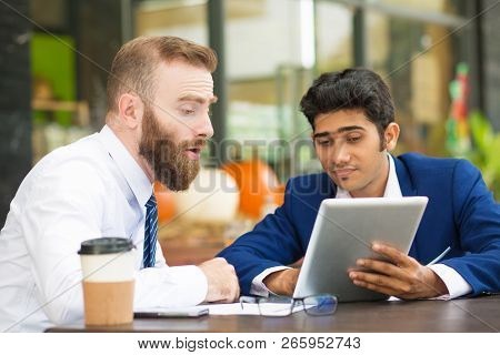 Shocked Bearded Man Viewing Online Presentation With Colleague In Cafe. Frowning Manager Looking At 