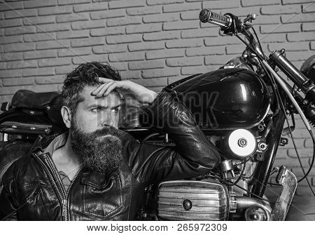 Bikers Lifestyle Concept. Man With Beard, Biker In Leather Jacket Near Motor Bike In Garage, Brick W