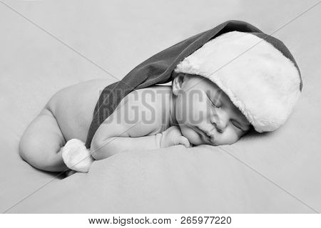 A Naked Newborn Baby Sleeps In A Christmas Hat.