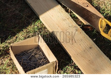 Box Of Nails, Boards, Hand Saw Lying On The Grass