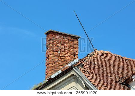 Cracked Broken Red Brick Chimney Next To Metal Leaning Lightning Rod On Top Of Abandoned Old Buildin