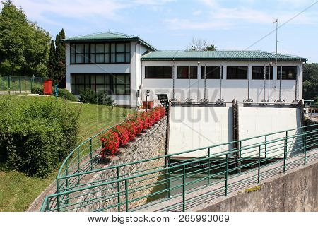 Small Dam Used To Regulate And Direct Water To Building Behind Used As Hydropower Plant With Freshly