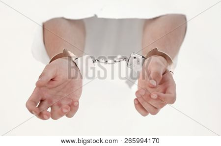 Handcuffs on the hands of a man breaking a paper wall