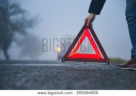 Traffic Problem In Thick Fog. Driver Putting Warning Triangle Behind His Broken Car.