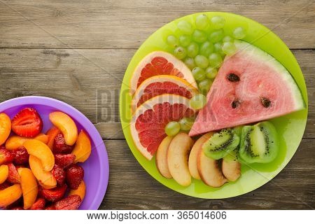 Sliced Fruit On A Borwn Wooden Background. Sliced Fruit On A Light Green Plate Wit Fruits On A Purpl