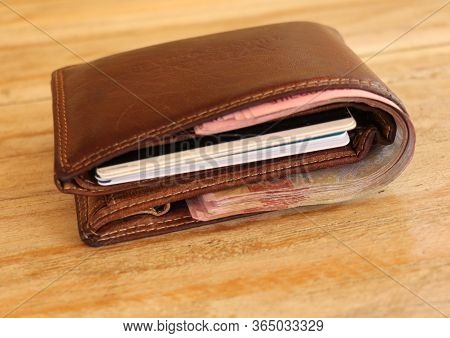 Brown Leather Wallet Full Of Banknotes And Credit Cards. Men's Wallet On A Wooden Table. Money In A 