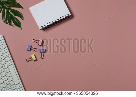 Top View With The Keyboard And Notebook On Pink Backgroup. Cluttered Office Desk Background.