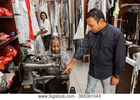 Small Business Owners Of Local Dry Cleaning Franchise Advising Staff About Clothing Repair