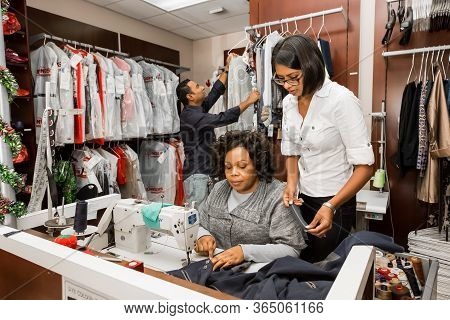 Small Business Owners Of Local Dry Cleaning Franchise Advising Staff About Clothing Repair