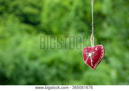 Isolated Handmade Cotton Fabric Heart Hanging On Bast String On Green Grass Background. Red Fabric H