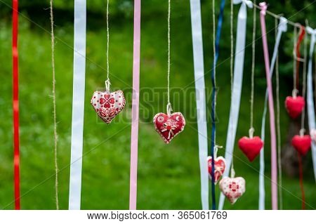 Seven Handmade Cotton Fabric Heart In Line With Ribbons Hanging On Bast String On Tree On Green Gras