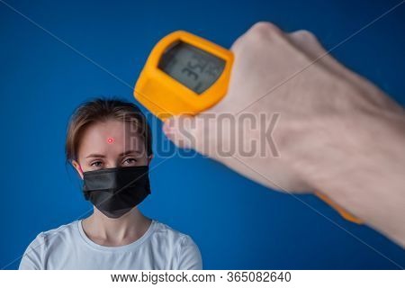 Man Hand Holding Yellow Pyrometer And Measuring Temperature Of Woman In Medical Face Mask Looking At