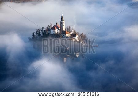 amazing panorama of Lake Bled Blejsko Jezero on a foggy morning with the Pilgrimage Church of the Assumption of Maria on a small island and Bled Castle and Julian Alps in backgroud