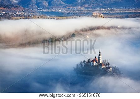 amazing panorama of Lake Bled Blejsko Jezero on a foggy morning with the Pilgrimage Church of the Assumption of Maria on a small island and Bled Castle and Julian Alps in backgroud