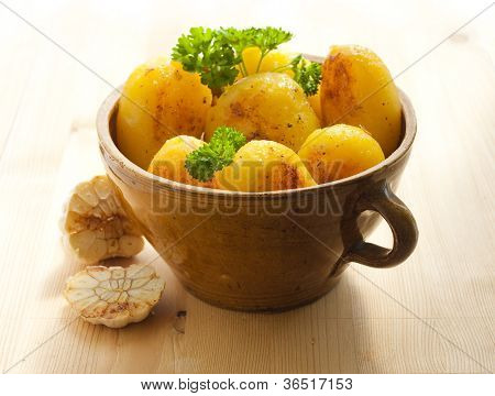 Clay pot fuld af kartofler og et hoved hvidløg på tabellen træ.
