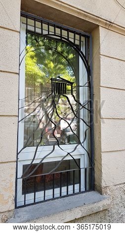 Unusual Metal Grating Protected White Window With Blurry Reflection In Window Glass. Details Of Clas