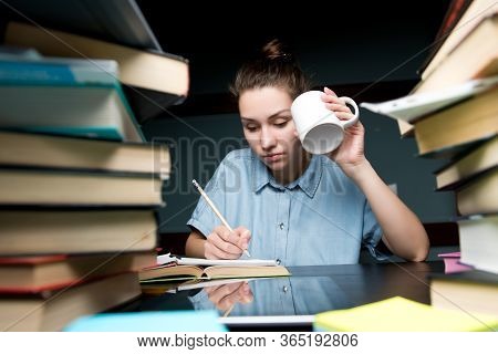 A Student Writes Knowledge In A Notebook And Drinks Coffee In The Late Evening. Girl Prepares For Un