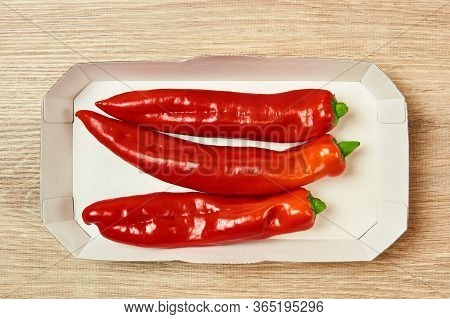 Three Pods Of Sweet Red Pepper Lie In A Cardboard Tray On The Table