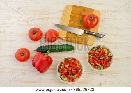 Two White Bowls With Fresh Salad Of Green Cucumbers, Red Tomatoes And Bell Peppers On Light Wooden S