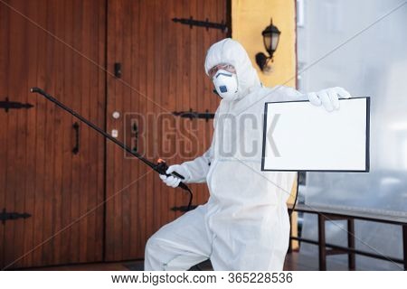 Coronavirus Pandemic. A Disinfector In A Protective Suit And Mask Sprays Disinfectants In House Or O