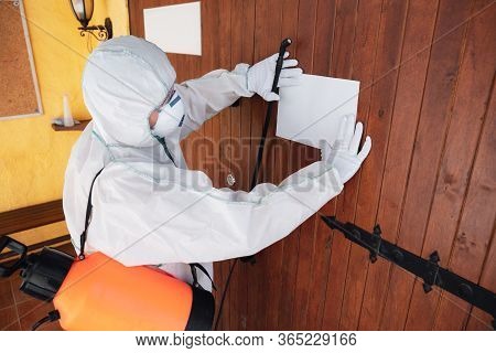 Coronavirus Pandemic. A Disinfector In A Protective Suit And Mask Sprays Disinfectants In House Or O