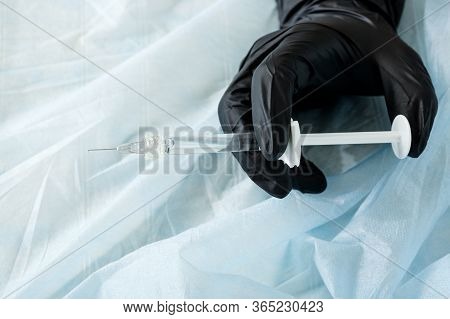Close-up Of The Hand In A Black Latex Glove With A Syringe With A Luer Lock On A Blue Spunbond Fabri